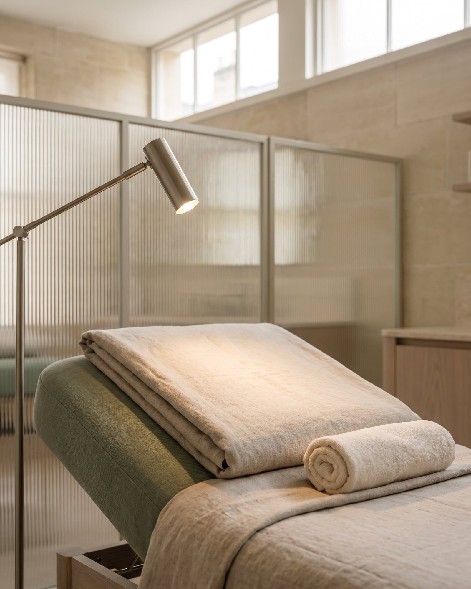 The head of a treatment bed with a folded linen blanket and a nickel lamp