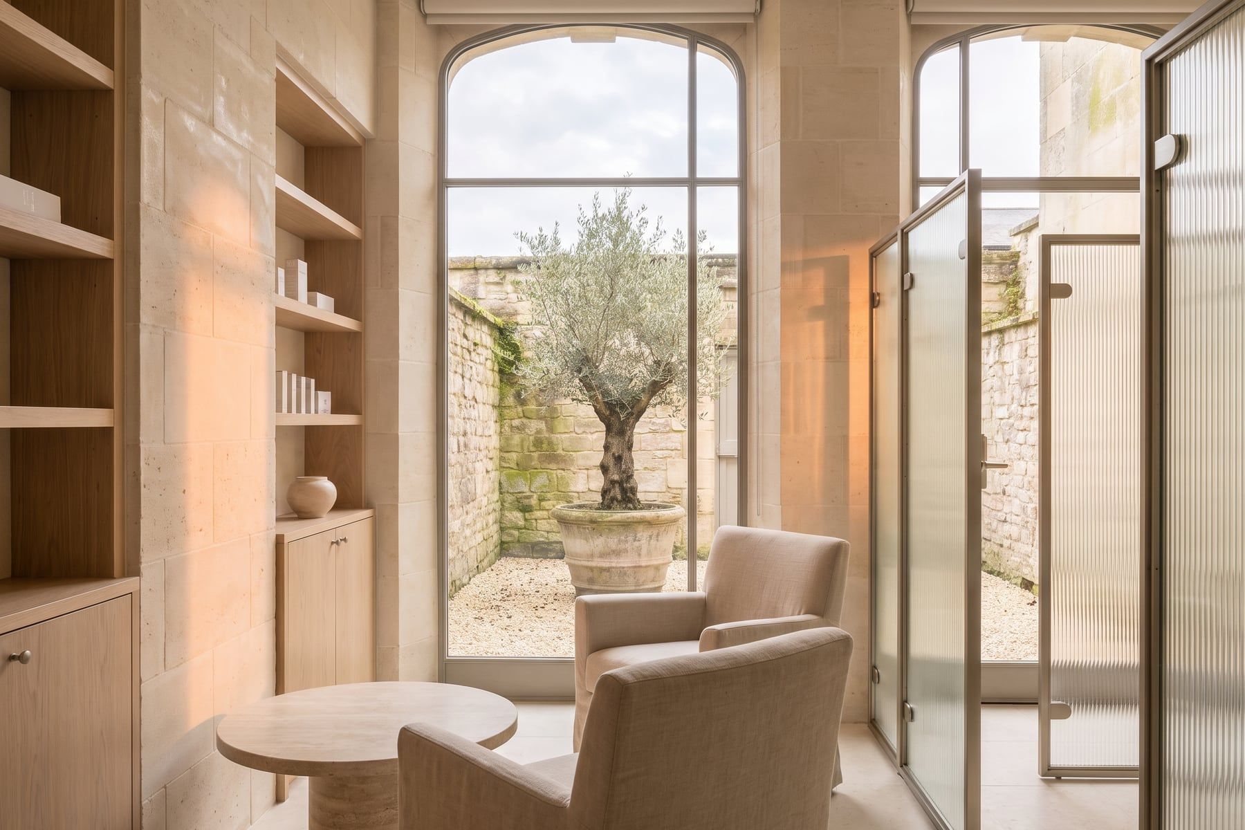 A walled courtyard with an olive tree seen through a tall window