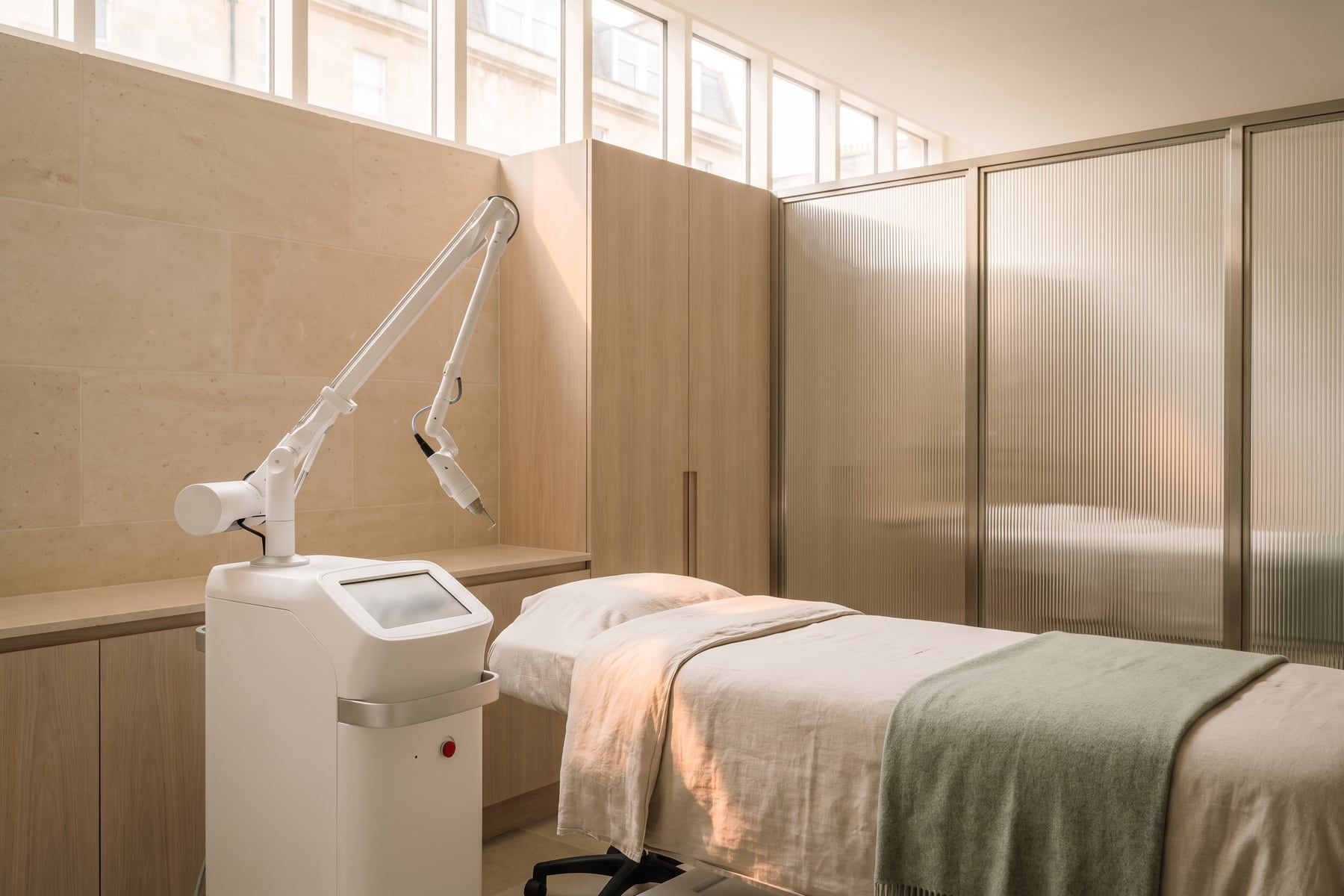 An unbranded white laser platform beside a linen-dressed treatment bed