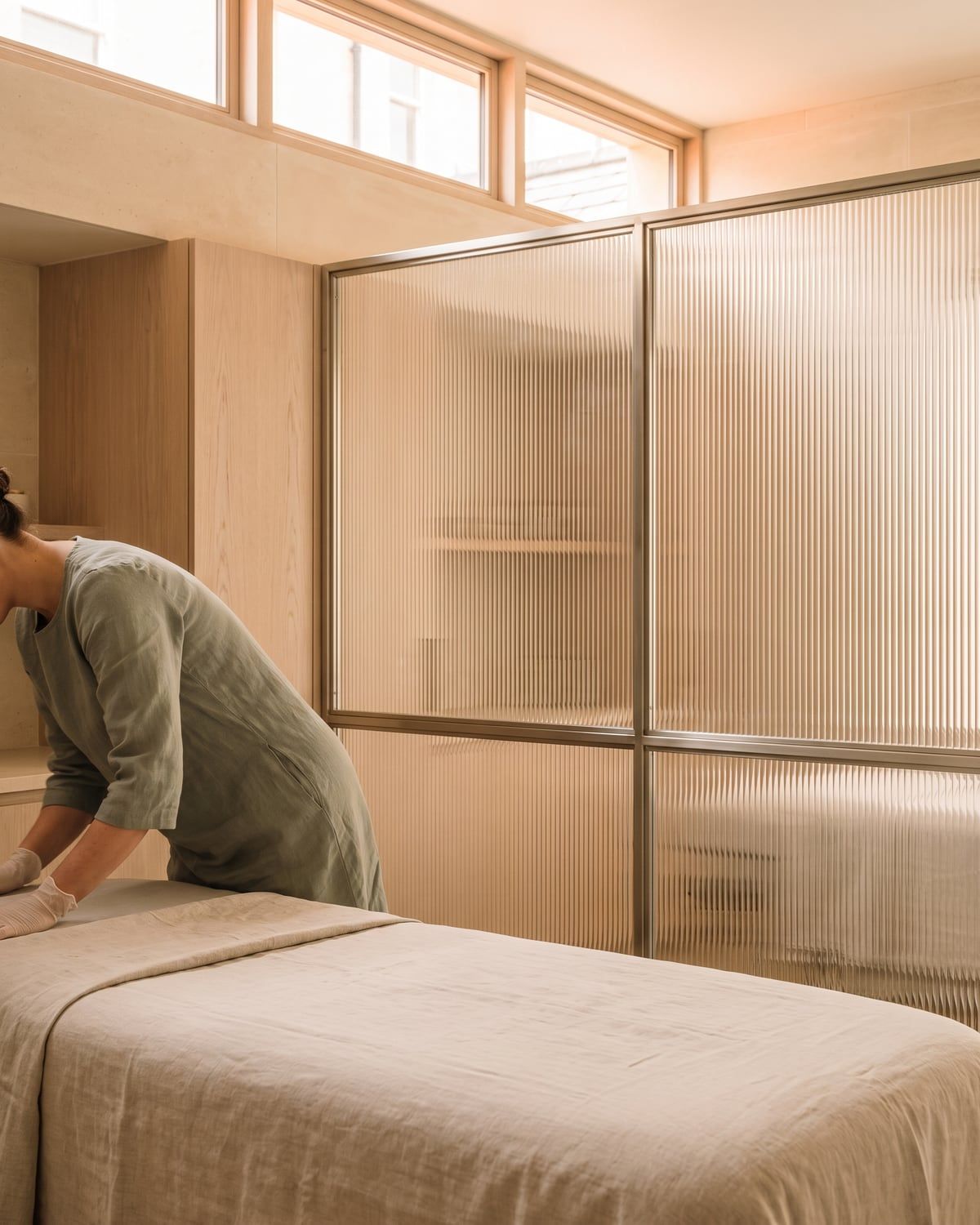 A practitioner seen from behind smoothing linen over a treatment bed