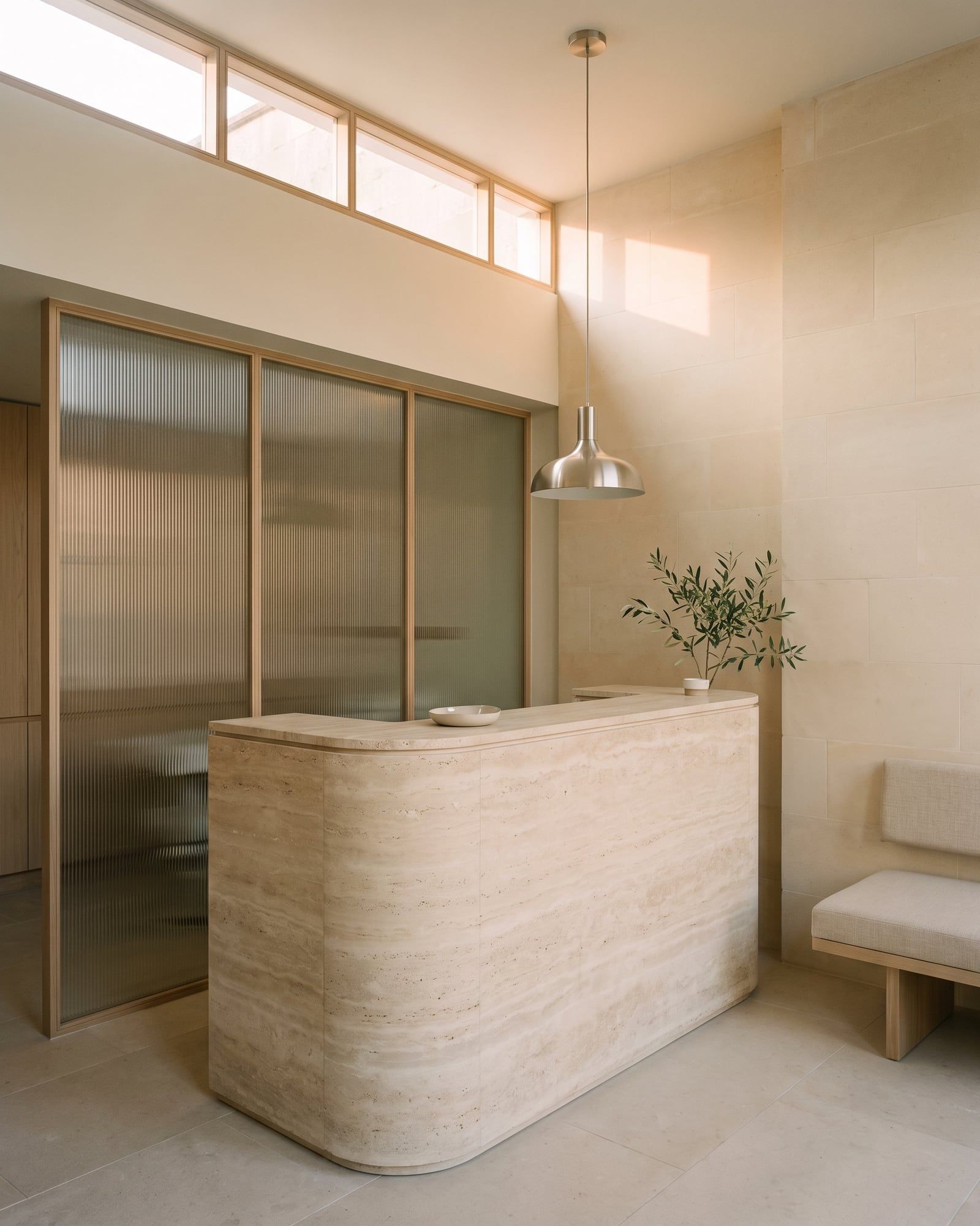 A rounded travertine reception desk under a nickel pendant light